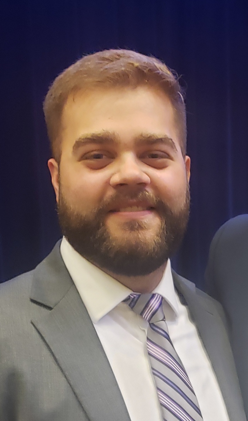 Man smiling into camera wearing suit with brown hair.