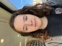 Woman with curly brown hair wearing a MSU bear crewneck looking smiles at camera with a library in background.